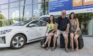Familie Holzwarth sitzt auf Gepäck vor einem E-Auto
