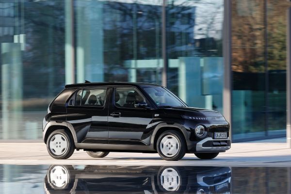 Ein schwarzer Hyundai Inster vor einem Glasgebäude.