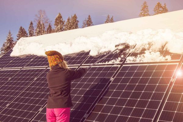 Frau entfernt im Winter Schnee von der PV-Anlage