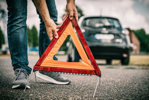 E-Auto Panne durch leeren Akku, Warndreieck wird aufgestellt.