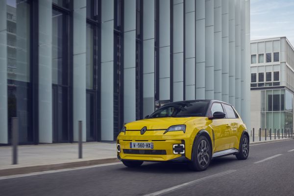 Gelber Renault 5 E-Tech Electric fährt eine Straße entlang.