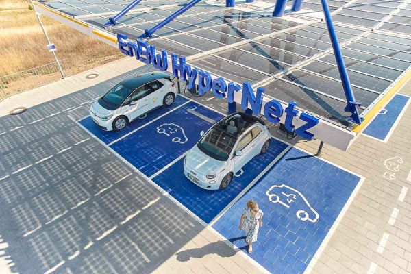 EnBW Schnellladepark. Zwei Autos werden gerade geladen und daneben läuft eine Frau.