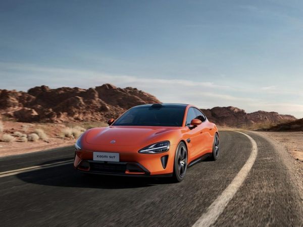 Xiaomi SU7 in Lava Orange fährt Landstraße entlang.
