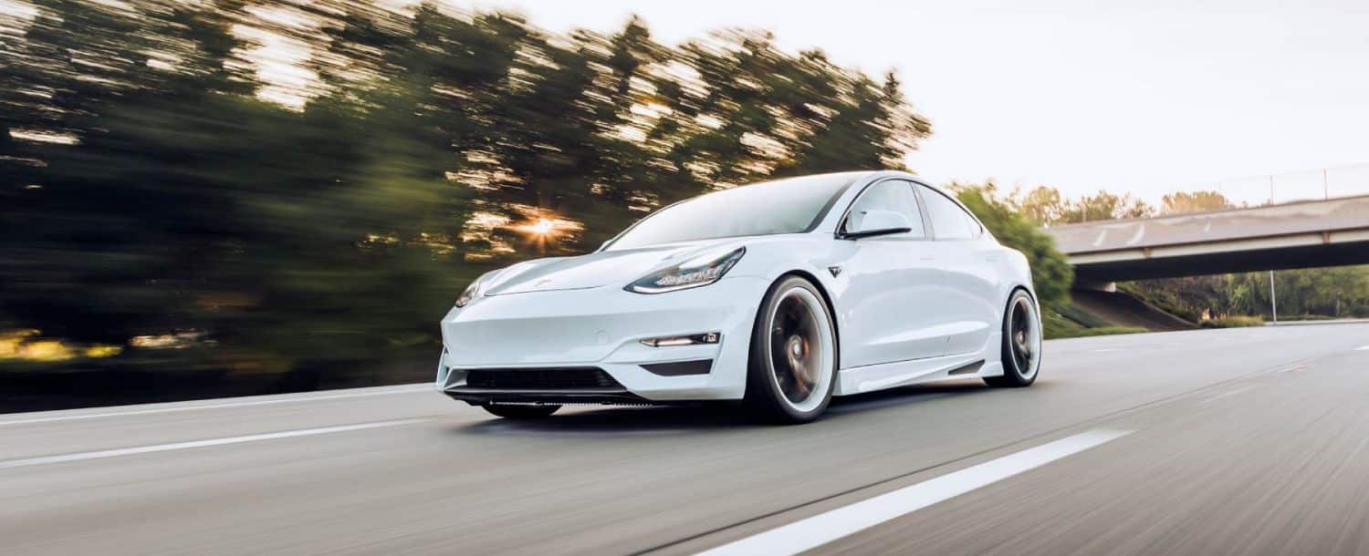 Weißer Tesla fährt Straße entlang.
