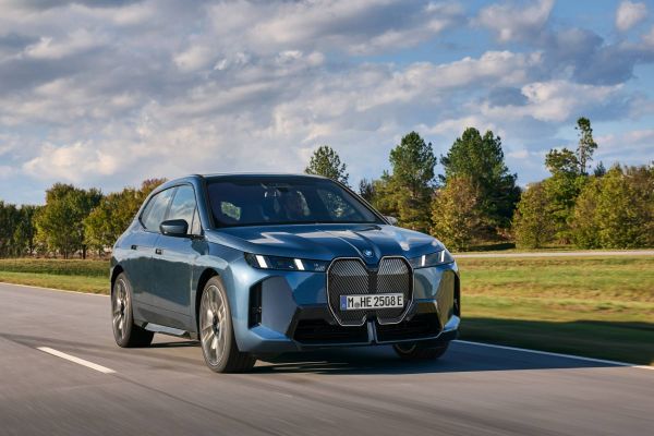 Ein dunkelblauer BMW IX fährt an einem Feld entlang.