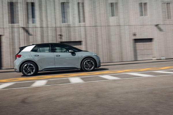 Ein VW E-Auto fährt entlang einer Beton-Häuserfassade.