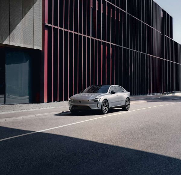 Ein silberfarbener Volvo ES90 fährt an einem Bürogebäude vorbei. 