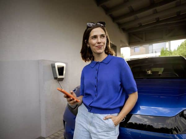 Frau mit Handy in der Hand lädt ihr blaues Elektroauto an einer Wallbox