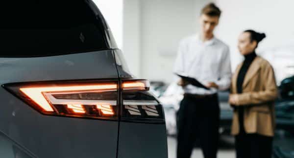 Autohändler steht mit einer Kundin im Autohaus vor einem E-Auto