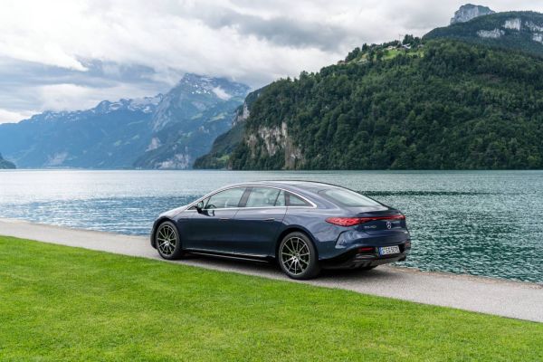 Mercedes EQS 450+ am Wasser entlang, vor einer Bergkulisse.